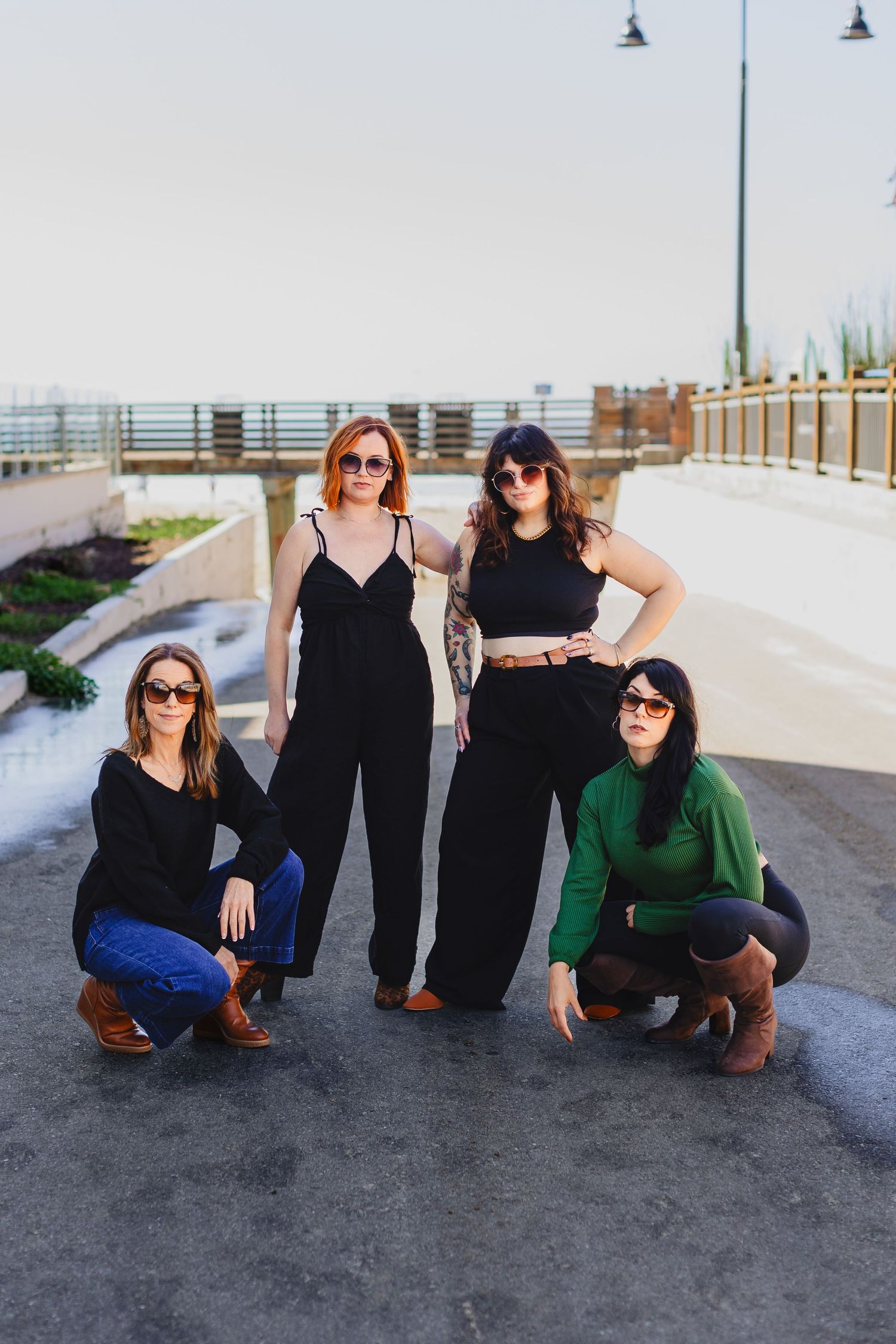 Four friends in stylish black outfits posing together on a waterfront path.