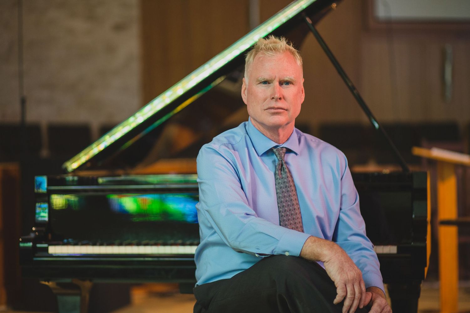 Professional musician sits at grand piano in performance hall.