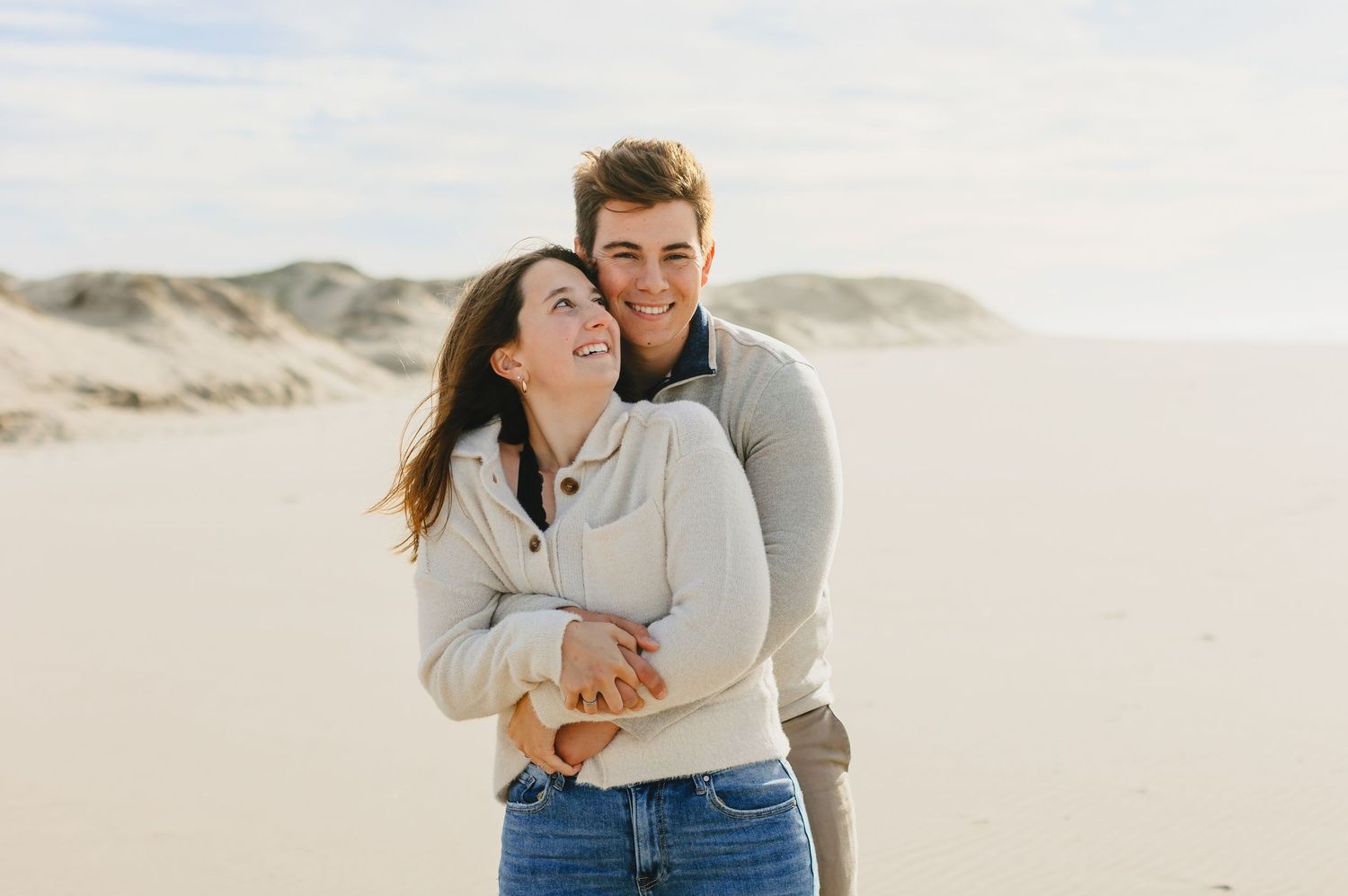 Couple embracing and laughing together on sandy beach dunes.