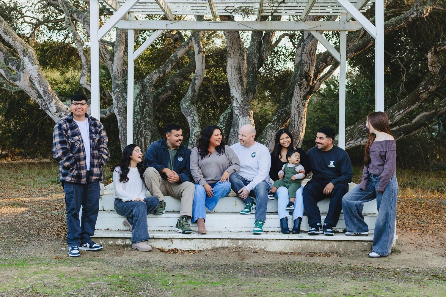 A casual group photo of people sitting together on a white wooden gazebo bench outdoors.