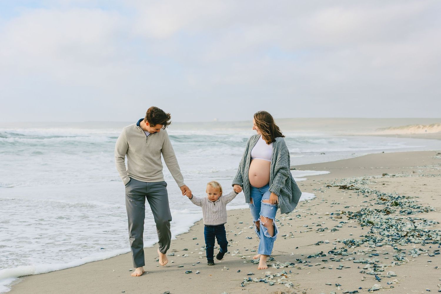 A family walks together along a beach shoreline on an overcast day.