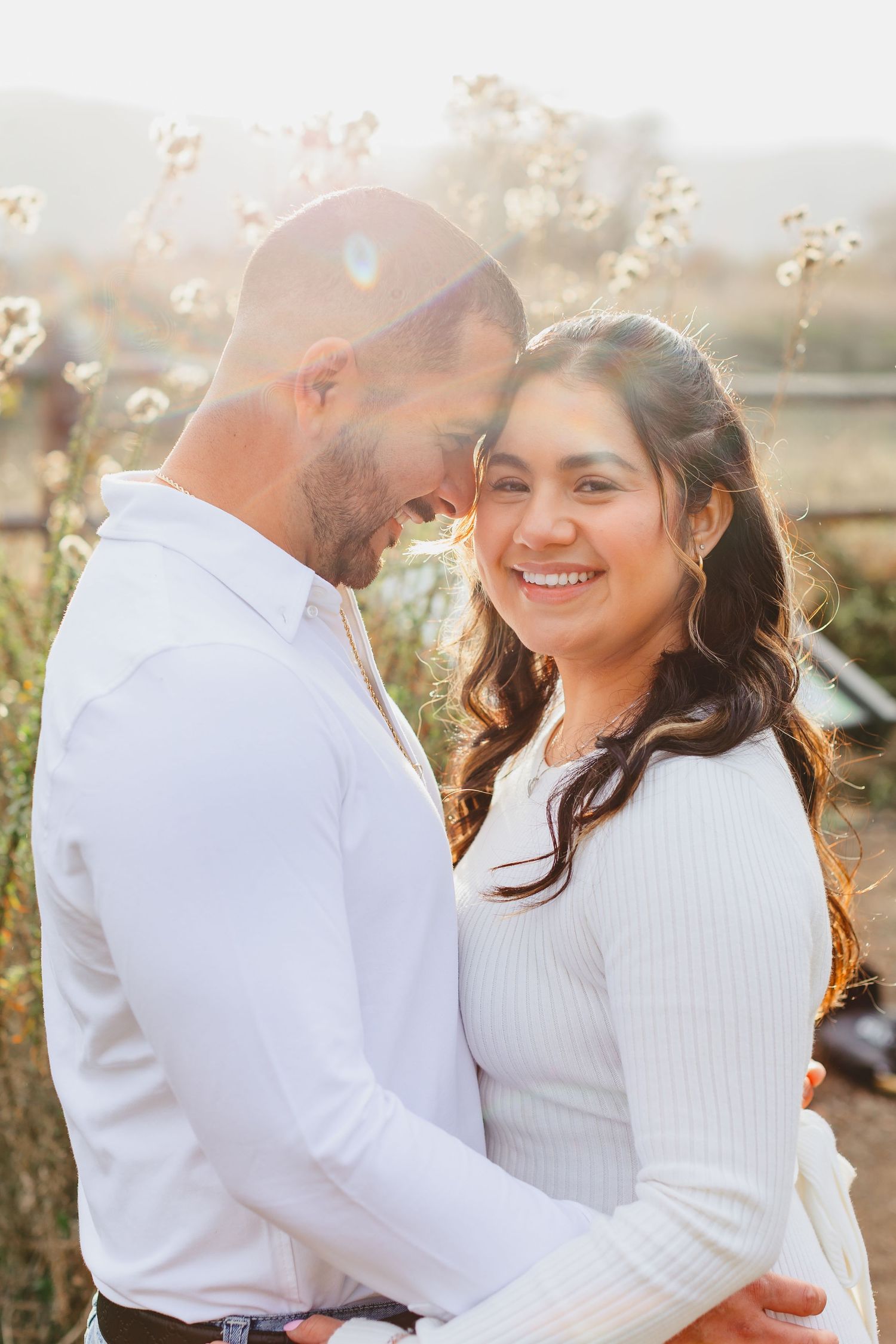 Couple sharing intimate moment in golden sunlit field with warm smiles.