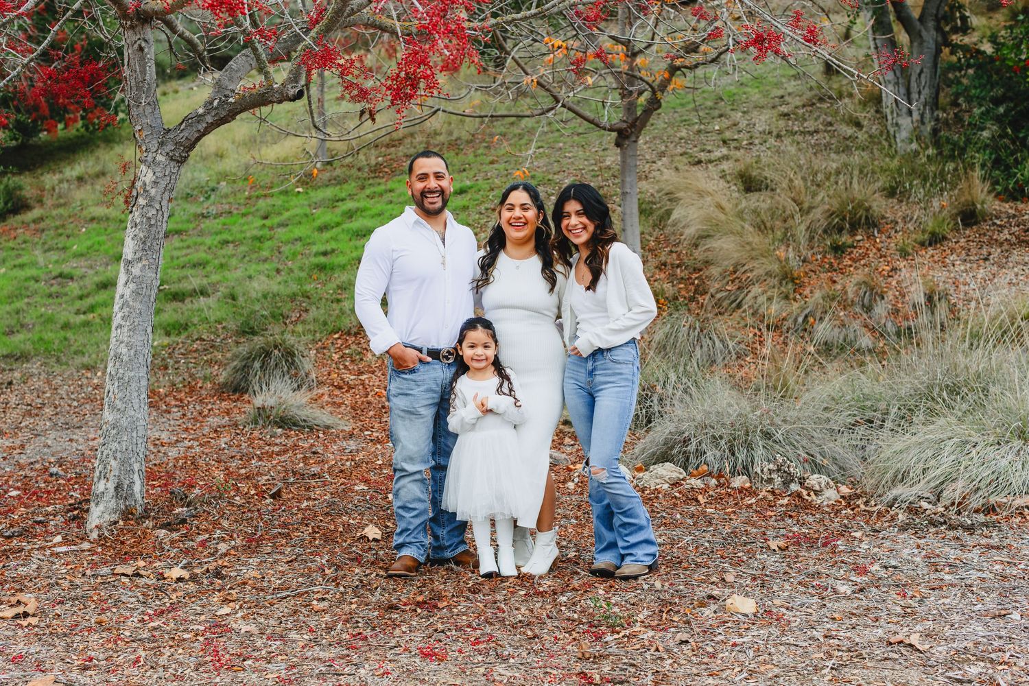 Family of four poses together under a red-berried tree in an autumn setting.