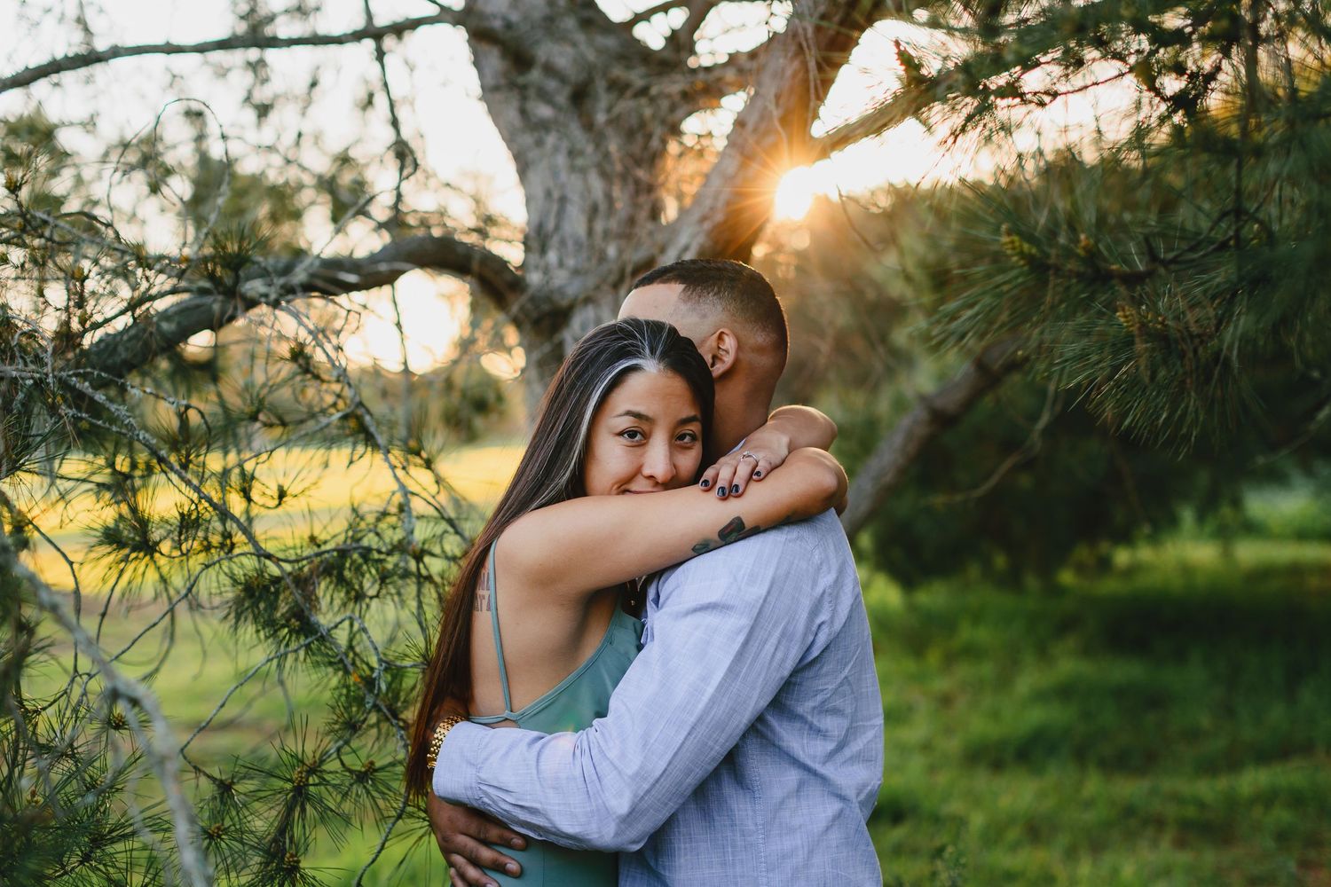 Couple embracing in nature with sun flare through trees.