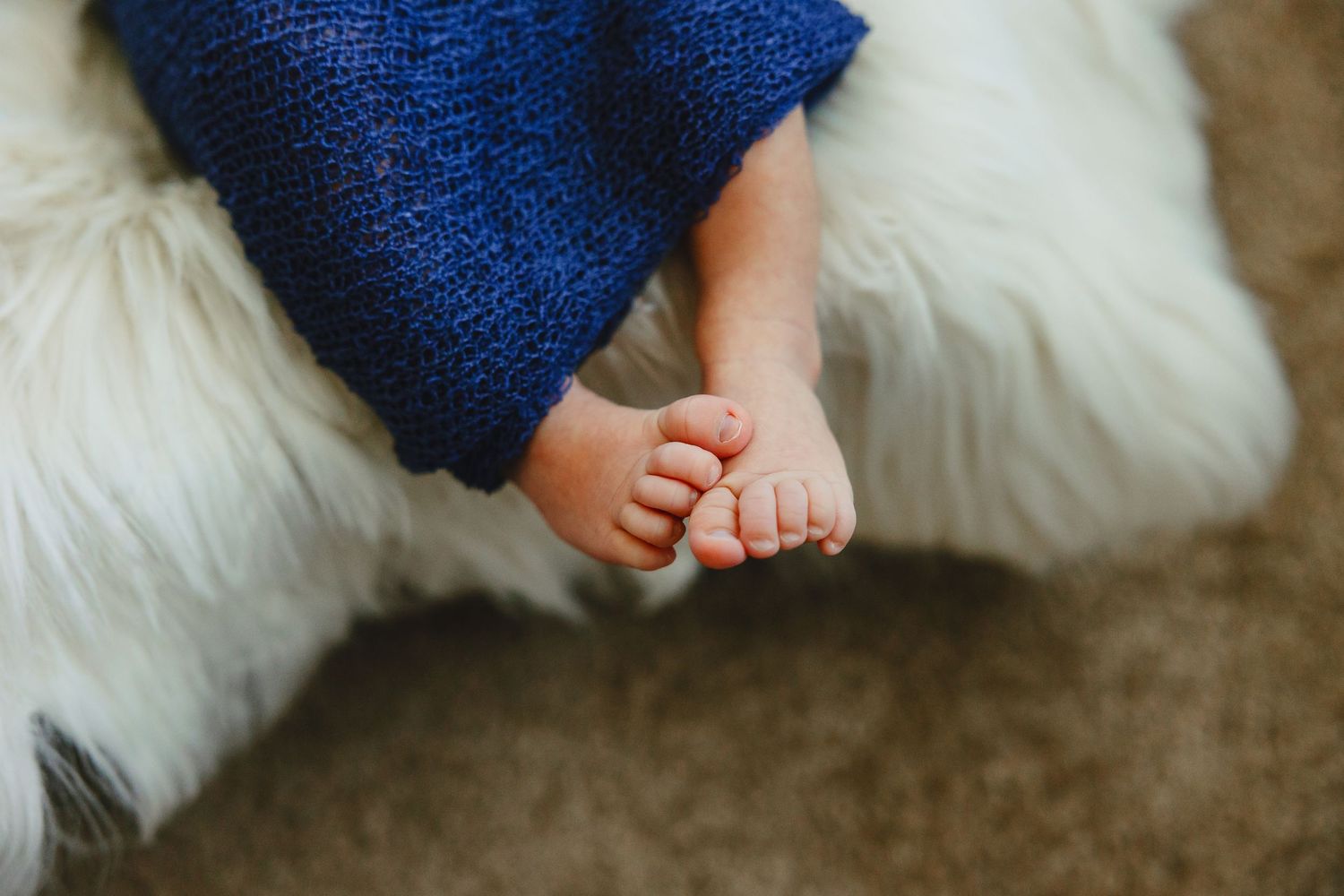 Small bare baby feet resting on soft white fur against a dark carpet background.