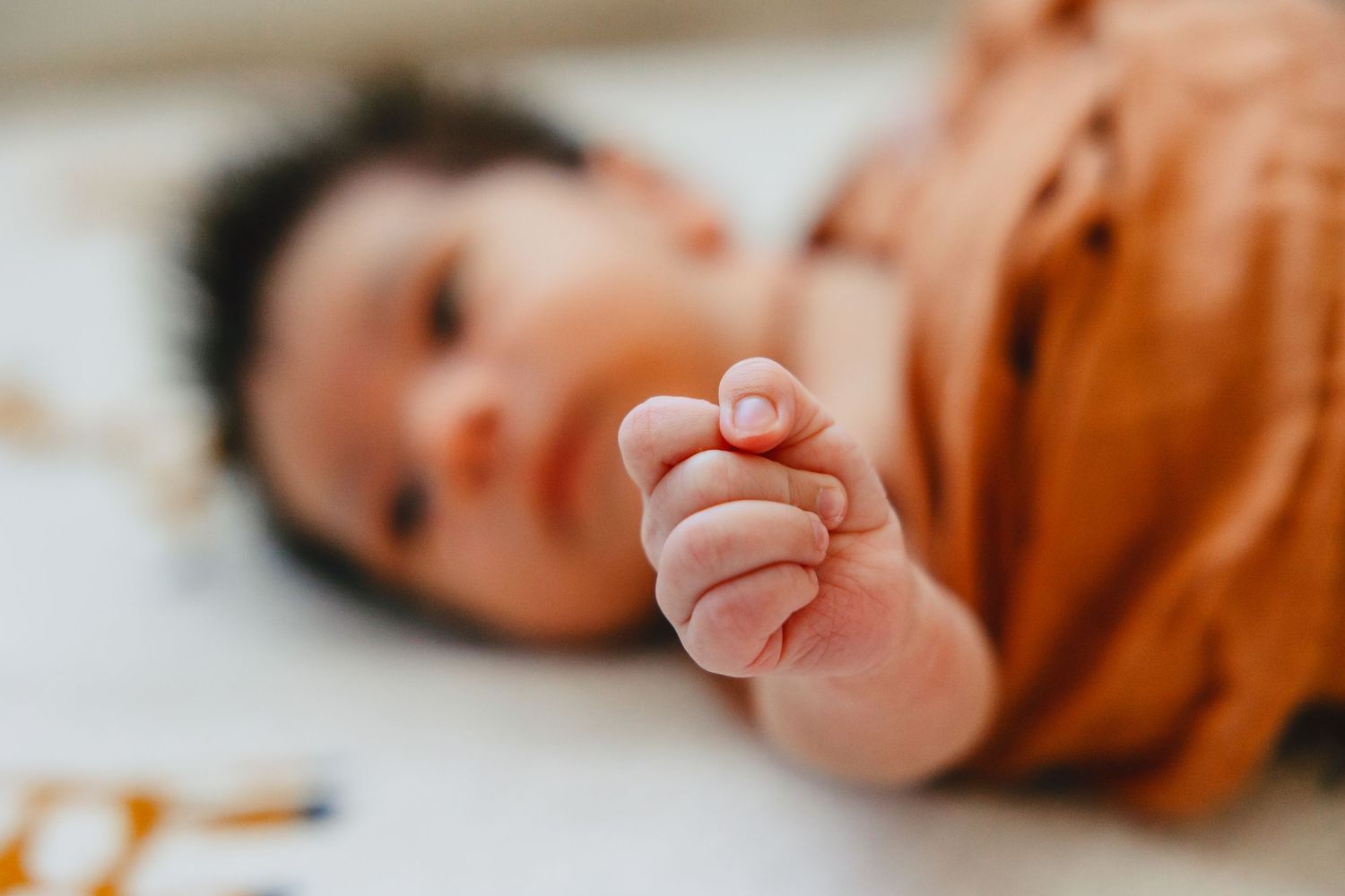 Close up of tiny baby hand with orange swaddle visible.