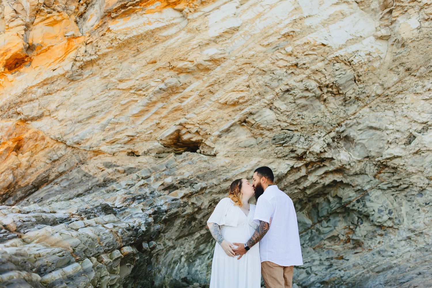 Intimate maternity photo of couple by rocky cliffside during golden hour.