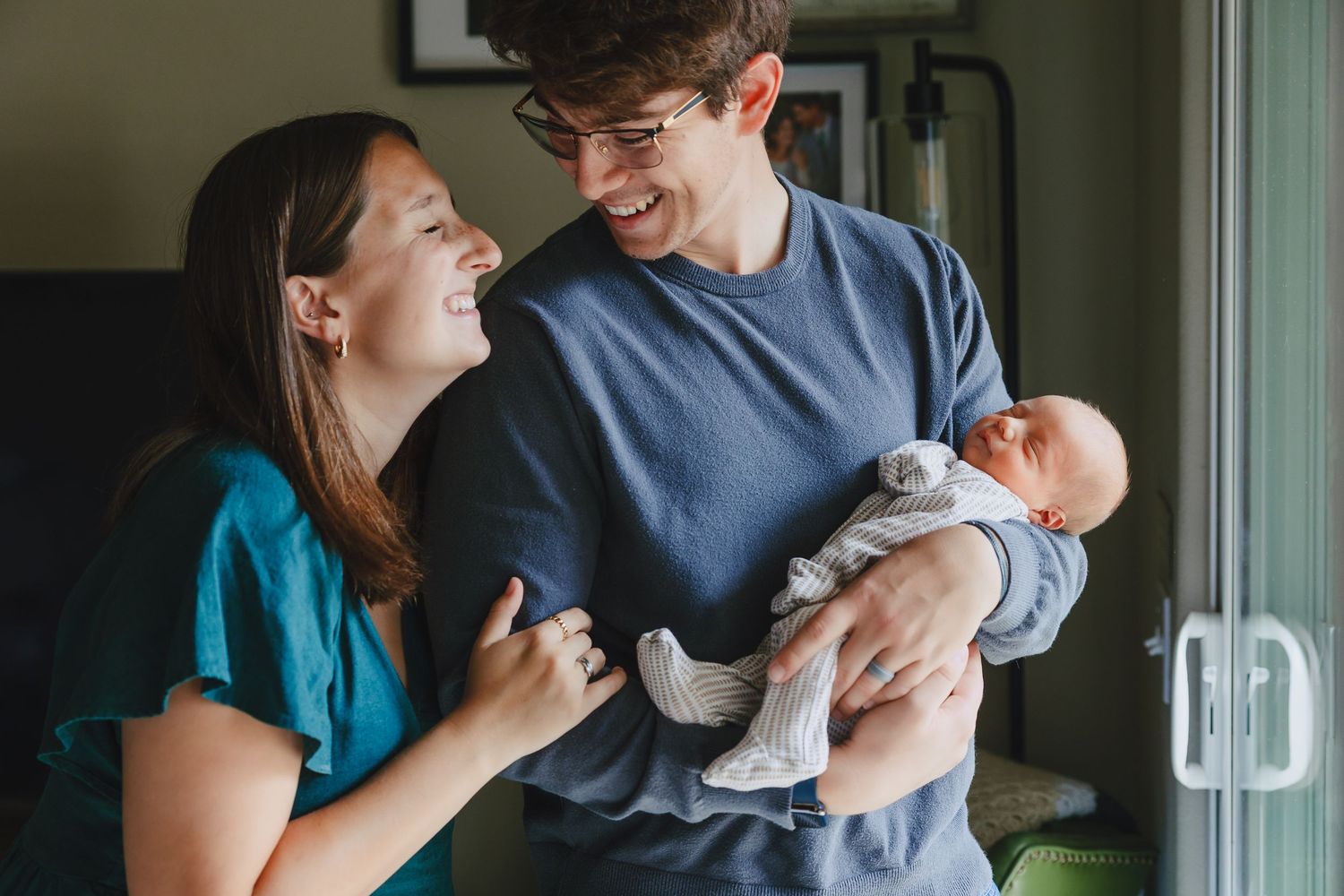 A couple in blue shirts share a tender moment looking at their newborn baby in a home setting.