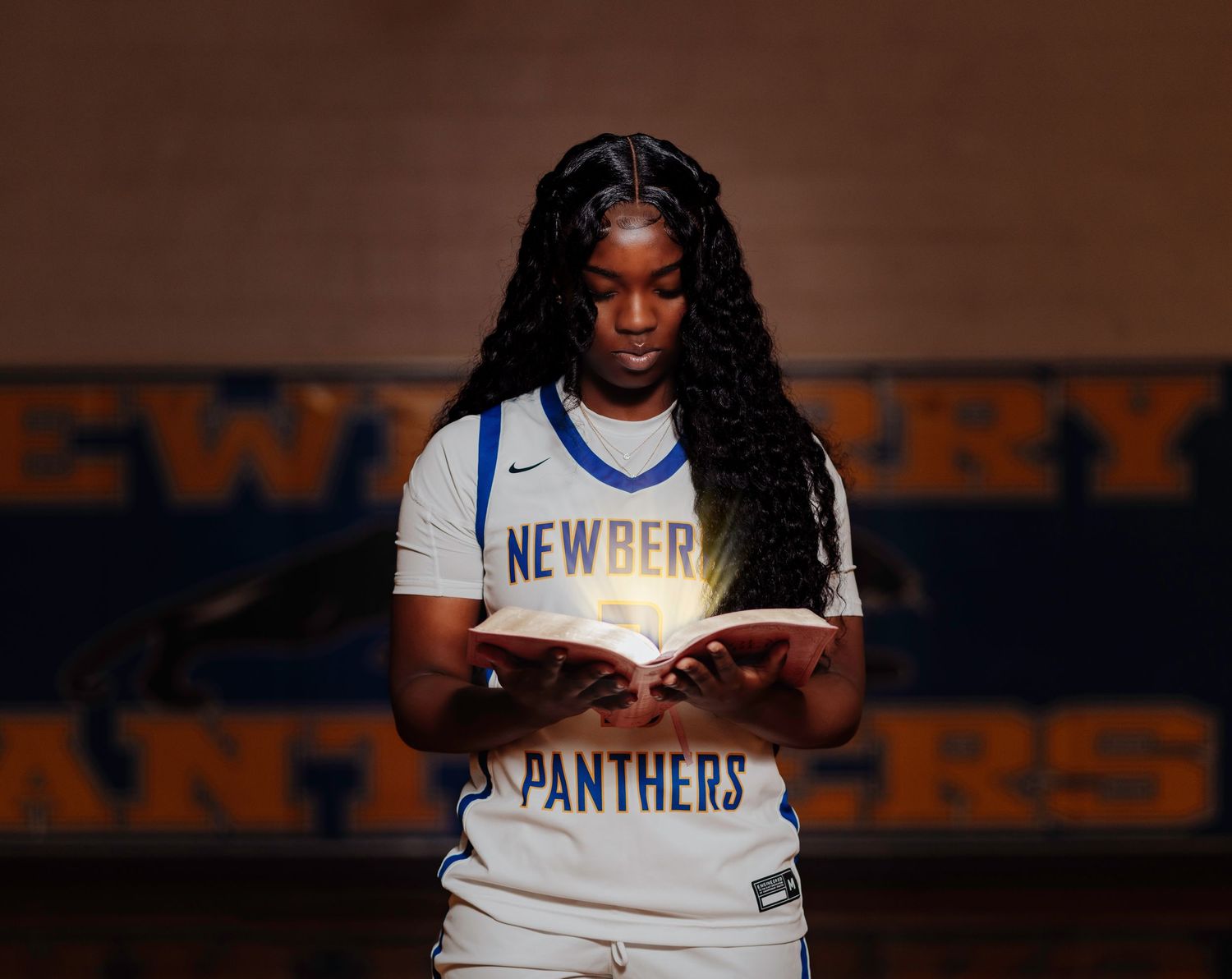 Student athlete in New Perry Panthers sports attire stands reading against dark background with school lettering.