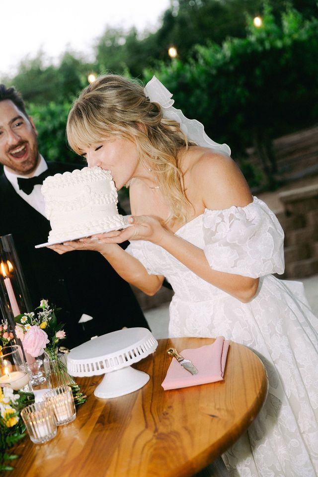 Playful moment as bride takes bite of wedding cake at reception.