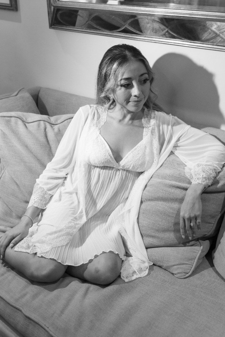 Figure rests on a couch in relaxed poses wearing white while soft shadows create a dreamy atmosphere.