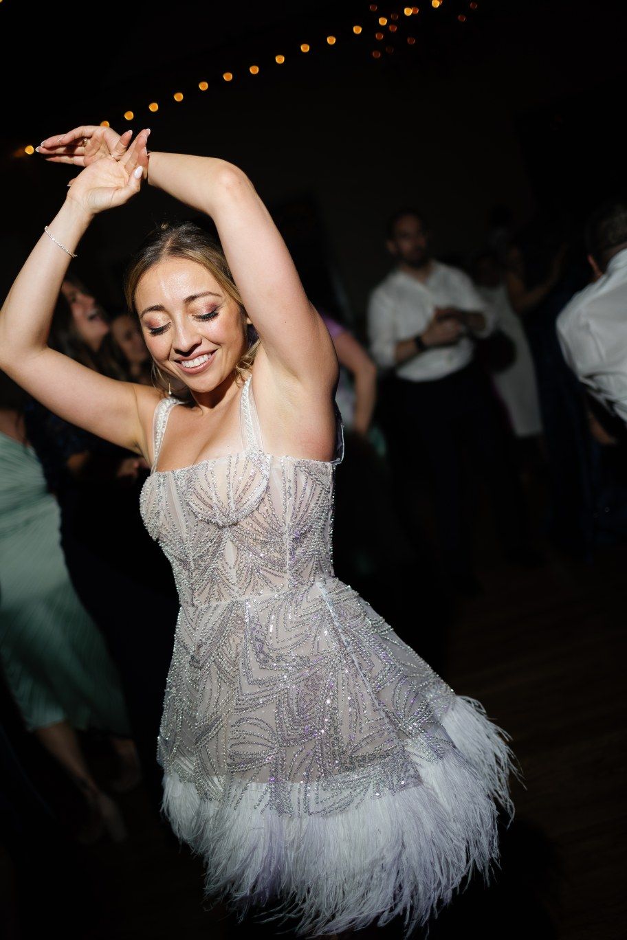 A bride in a feathered white dress dances joyfully at her wedding reception.