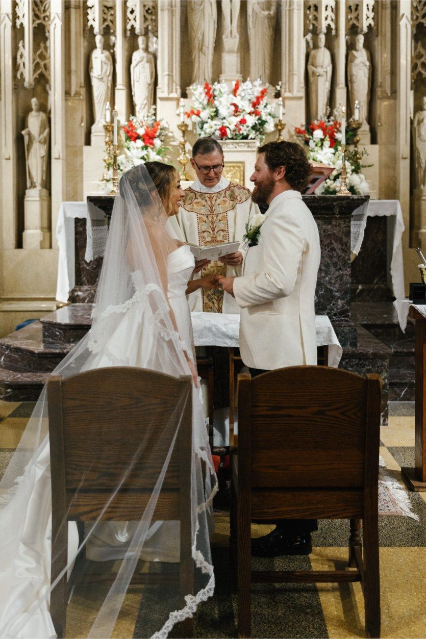 A wedding ceremony takes place in an ornate church with floral decorations and gothic architecture.