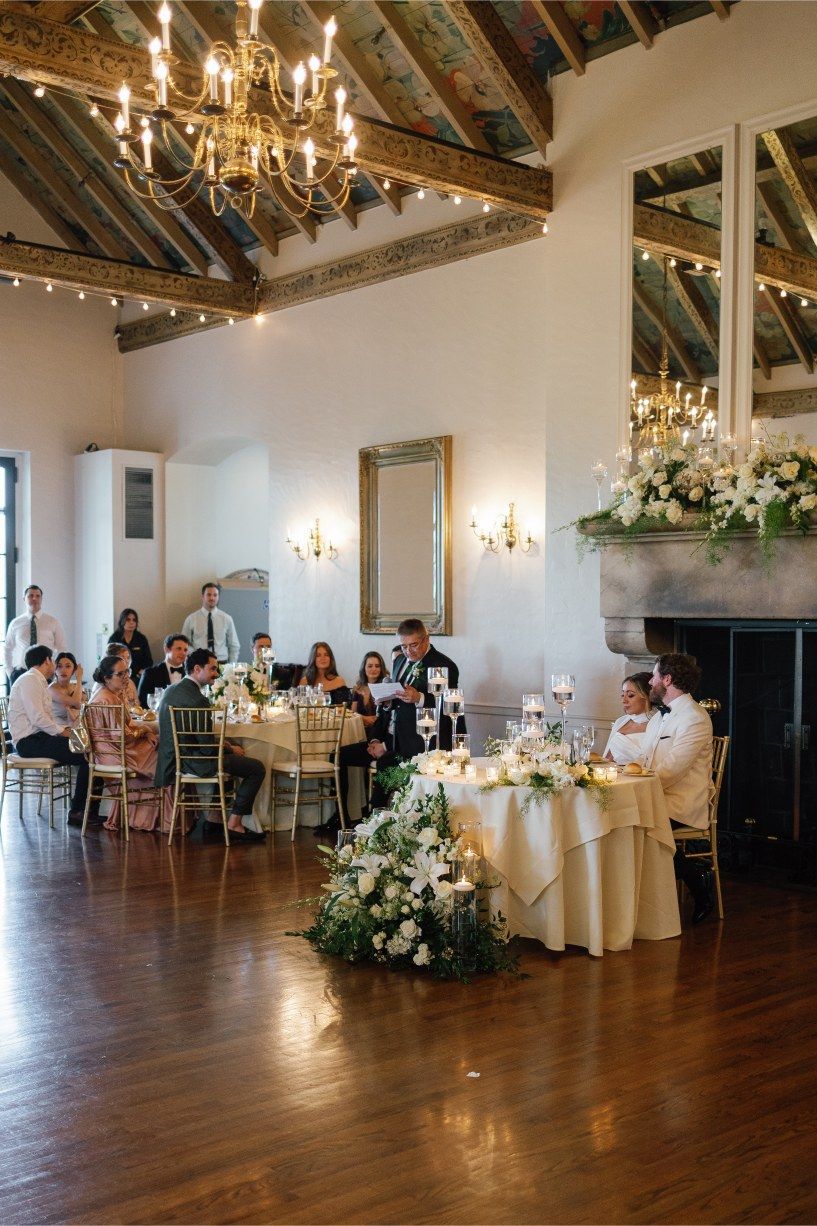 Wedding reception hall with vaulted ceiling, chandeliers and round tables set for dining.
