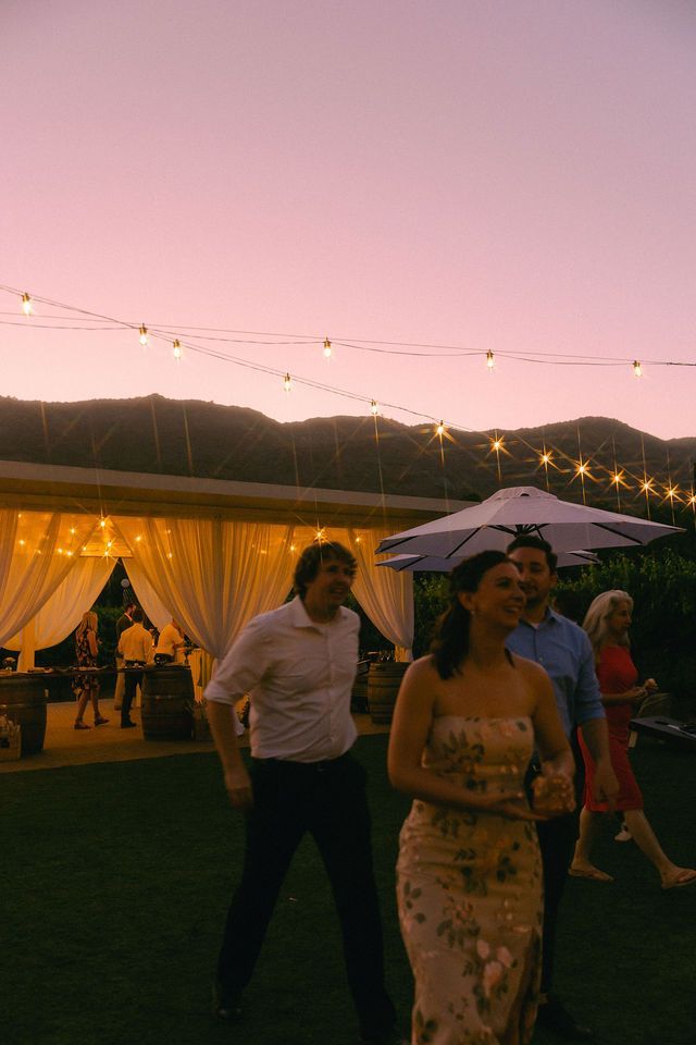 Guests dance under string lights at outdoor evening wedding reception.