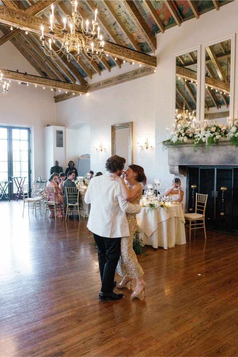 Couples dancing in a rustic reception venue with exposed wooden beams and chandeliers.