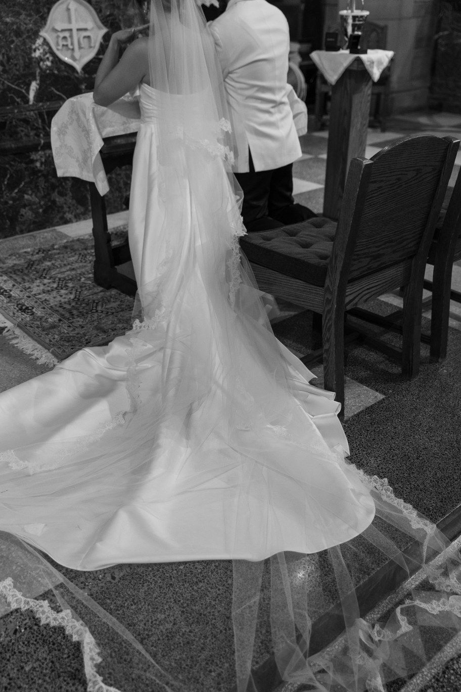 Black and white photograph of a flowing wedding dress train with delicate veil detail during a church ceremony.