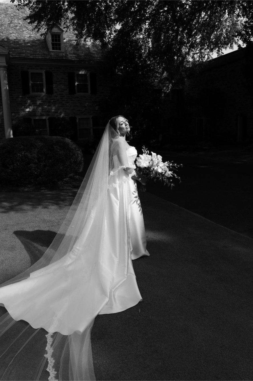 A flowing white wedding dress and veil billow ethereally in the breeze against a dark outdoor background.