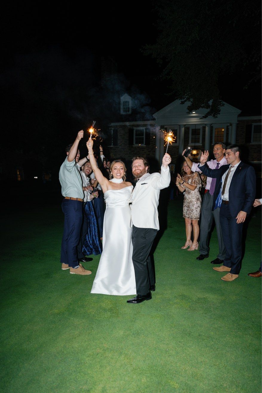 Wedding guests dancing together on a dark lawn with sparklers creating a festive atmosphere.