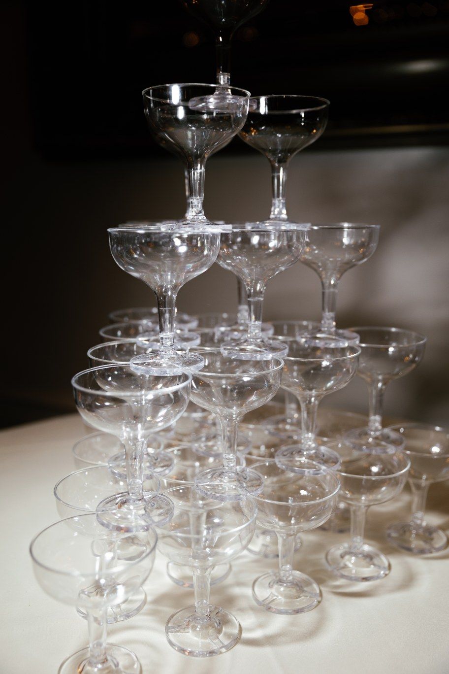 A pyramid of stacked champagne coupe glasses arranged in tiers on a white surface.