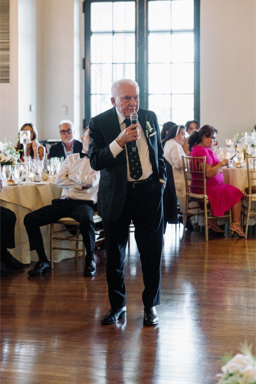 Speaker addressing guests during wedding reception in an elegant ballroom setting.