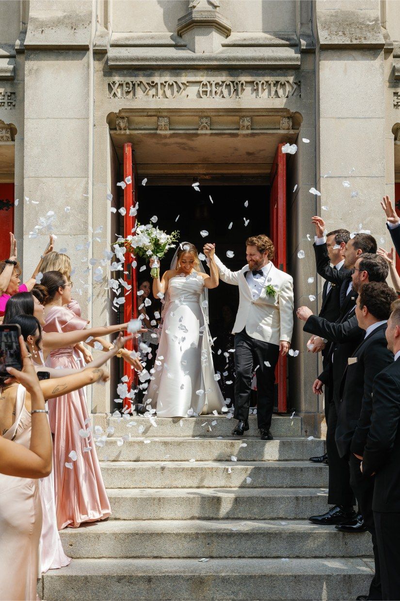 Wedding guests showering the newlyweds with rose petals as they exit the stone church building.