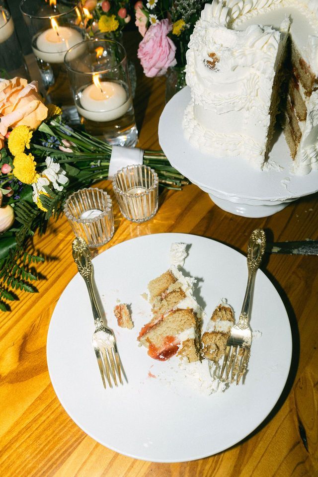 Elegant white wedding cake and slice served with lit candles and floral decorations.