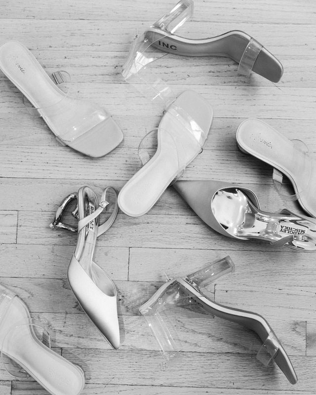 Collection of white and silver wedding shoes scattered on a light wooden floor.