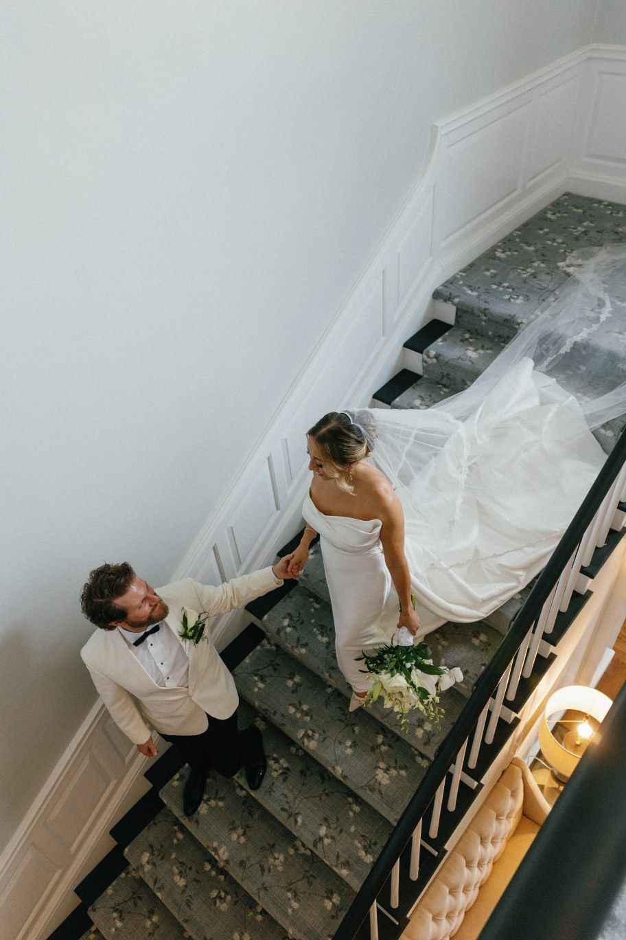 A couple descends an elegant staircase decorated with traditional white wainscoting and molding details.