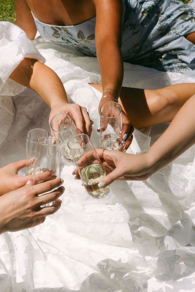 Hands holding champagne glasses over white fabric during a celebration.