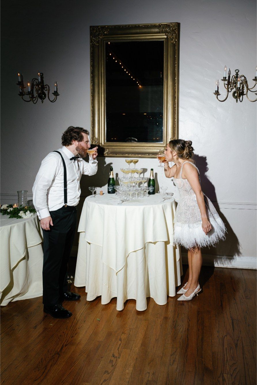 A playful wedding reception scene with elegant table settings, a large gold mirror, and wall sconces in the background.