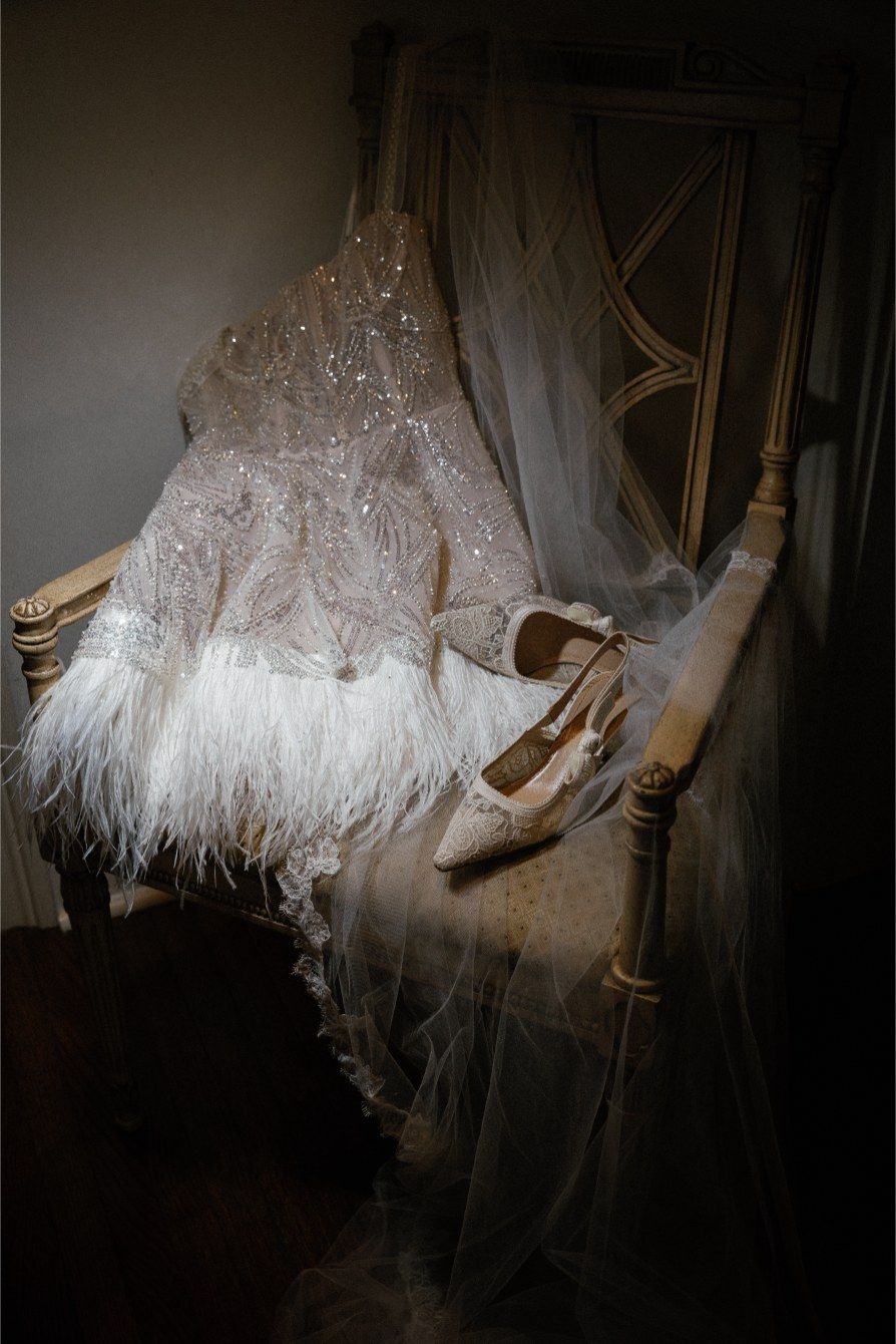 Close-up details of white feathers and elegant wedding shoes against a dark background in dramatic lighting.