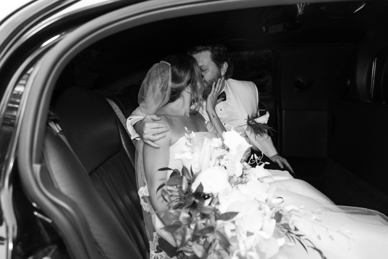 A couple shares an intimate moment in the backseat of a car during their vintage wedding celebration.