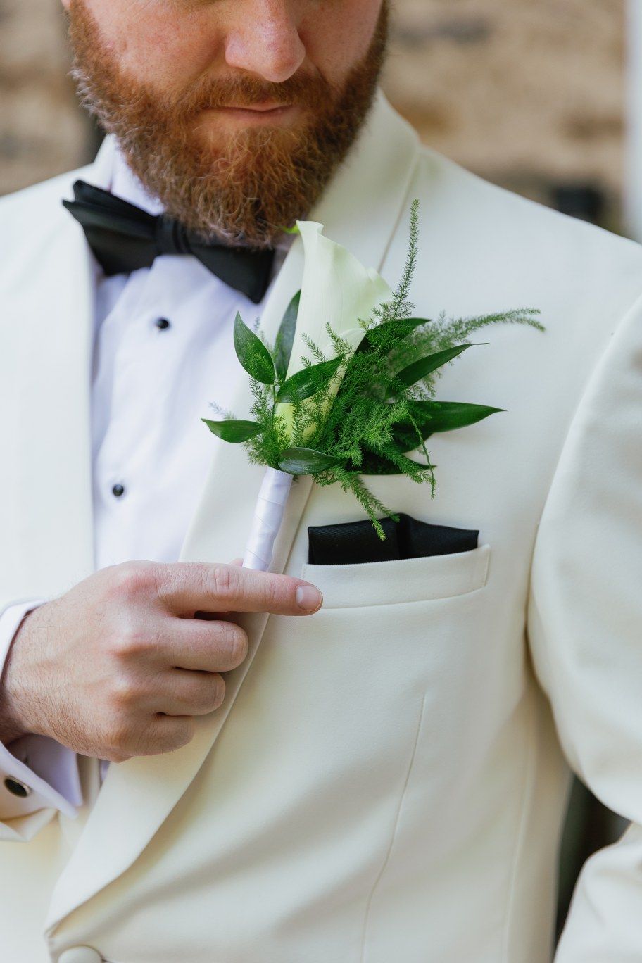 Close-up view of a white tuxedo jacket with a green fern and leaf boutonniere in the pocket.