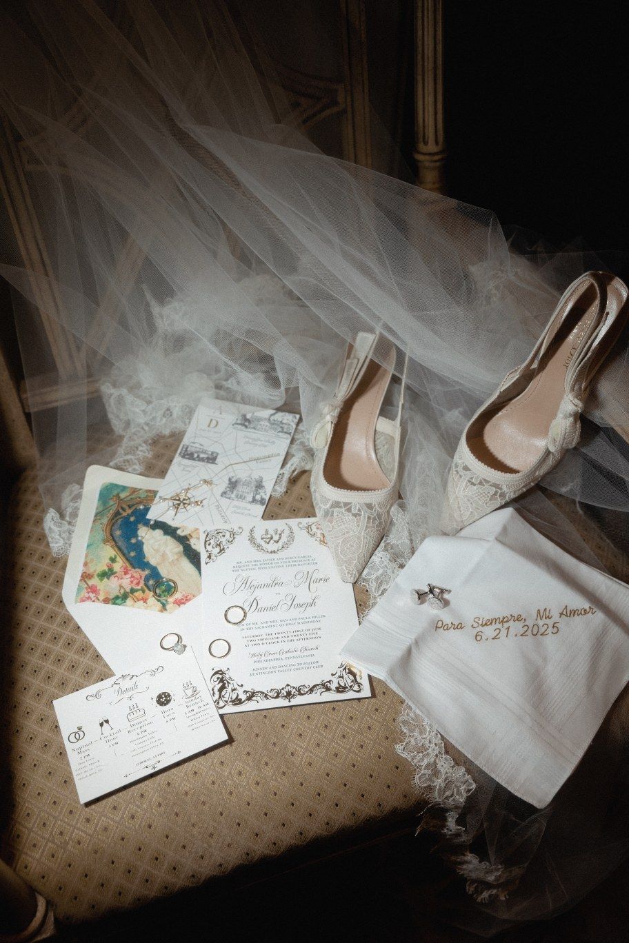 Wedding details including white slingback heels, invitation cards, veil and a small bag arranged on patterned carpet.