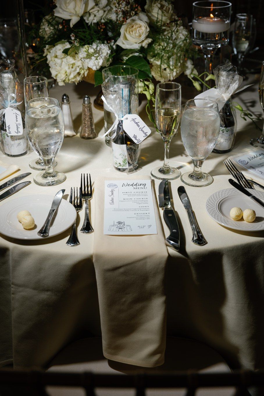 Elegant table settings with white linens, place cards, and floral centerpieces at a formal wedding reception.