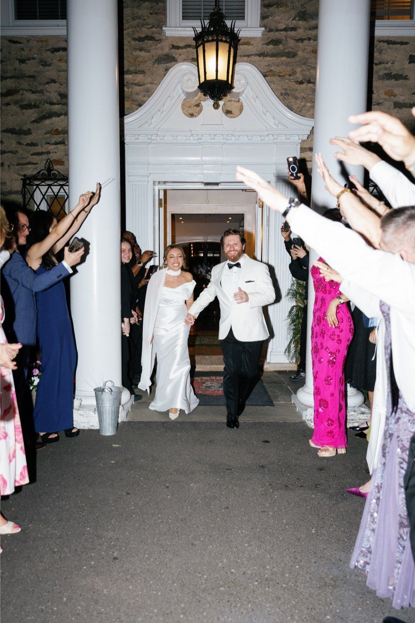 Wedding guests forming a departure tunnel with sparklers raised high outside a columned entrance.