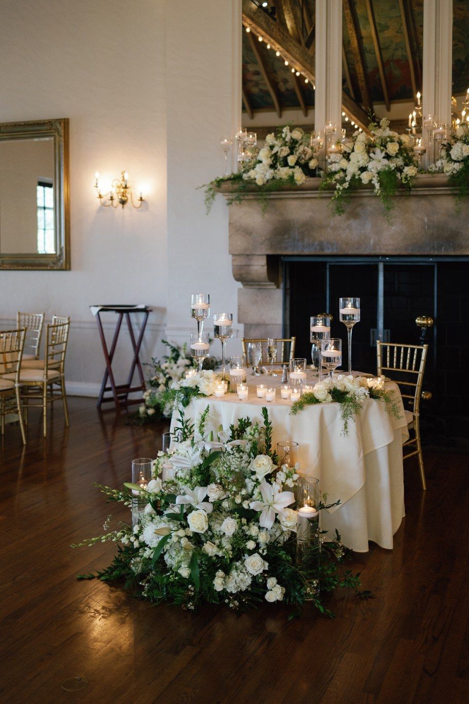 Elegant wedding reception venue with round tables dressed in white linens and floral centerpieces in a rustic ballroom space.