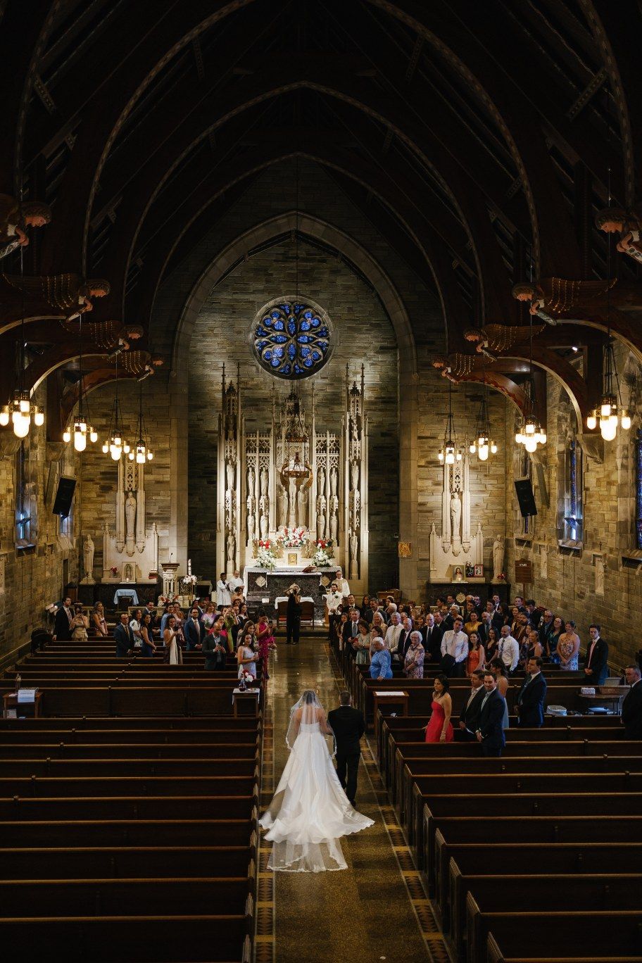A wedding ceremony in a grand cathedral with vaulted ceilings, stained glass windows, and guests seated in wooden pews.