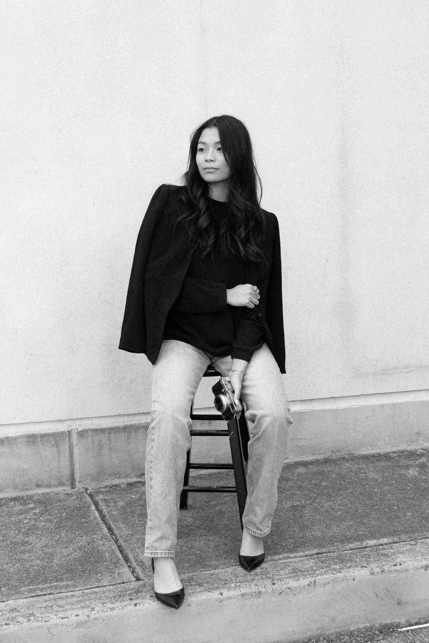 A series of four black and white photos showing someone in a black top and light pants sitting on a simple chair.