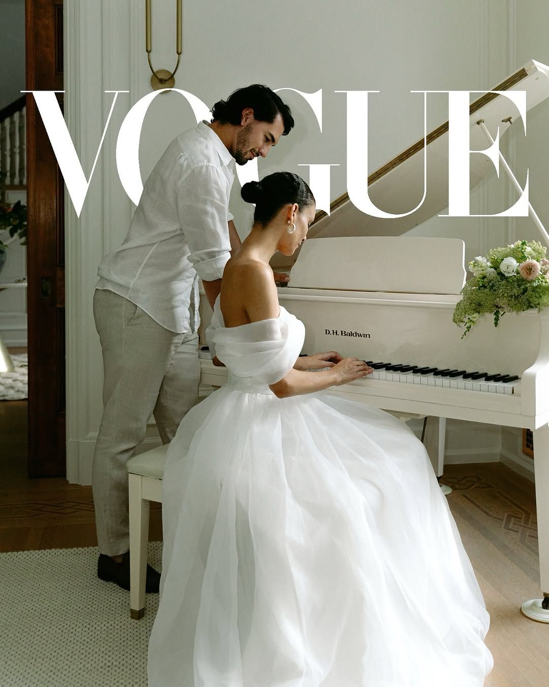 A couple in wedding attire share an intimate moment at a white piano in an elegant Vogue magazine photoshoot.