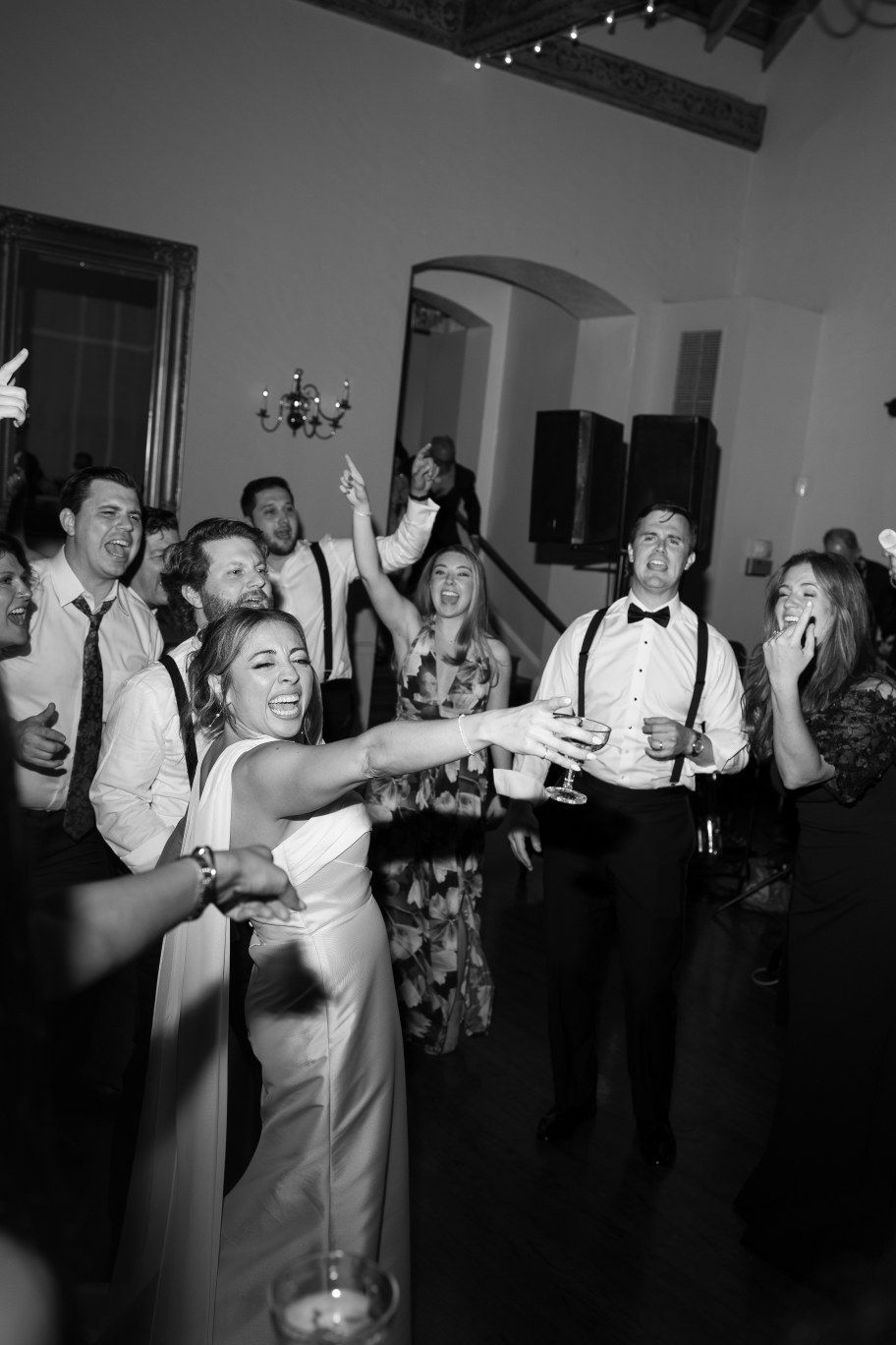 Wedding reception guests dancing and celebrating in formal attire at an indoor venue.