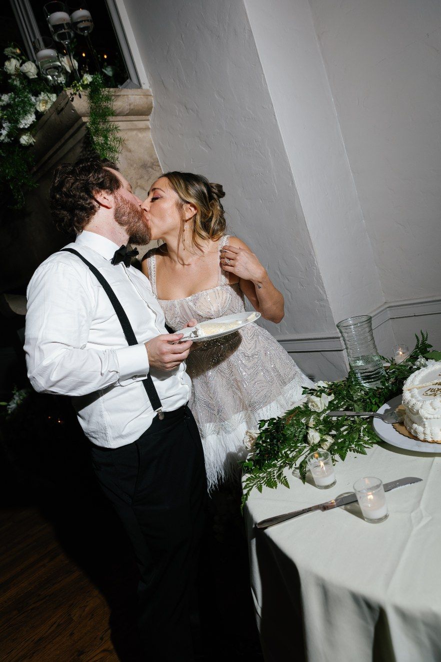 A couple in wedding attire shares an intimate moment while cutting their wedding cake together.