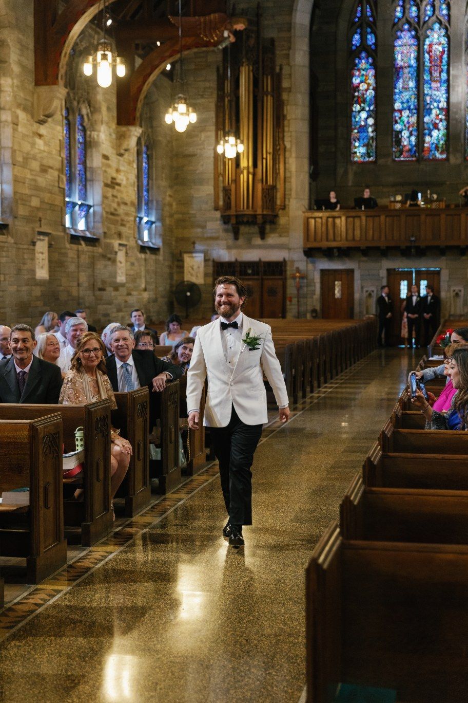 Interior view of a grand stone church with wooden pews and stained glass windows during a formal ceremony.