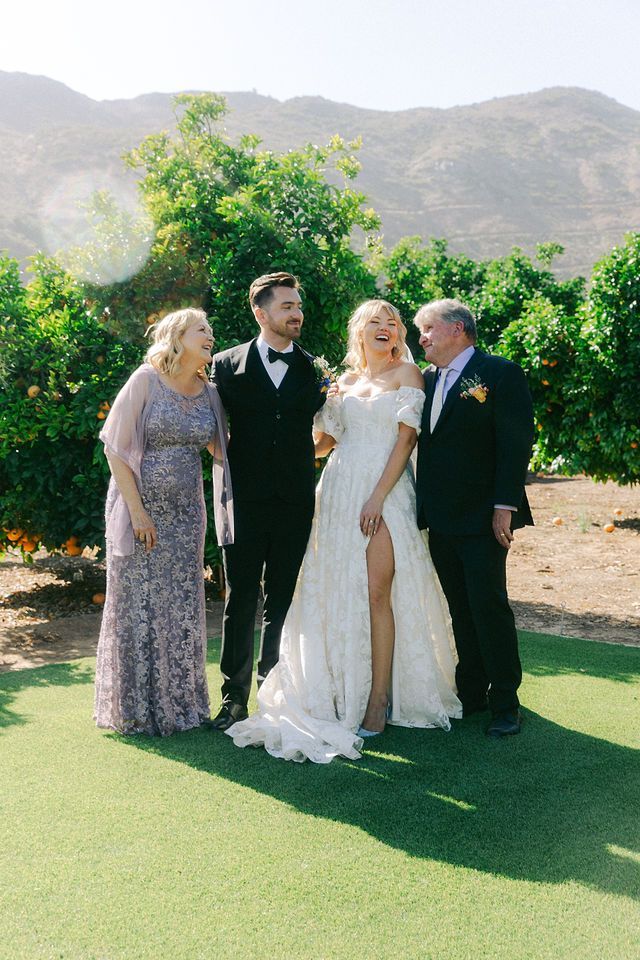 Wedding party poses on green lawn with mountain backdrop at outdoor ceremony.