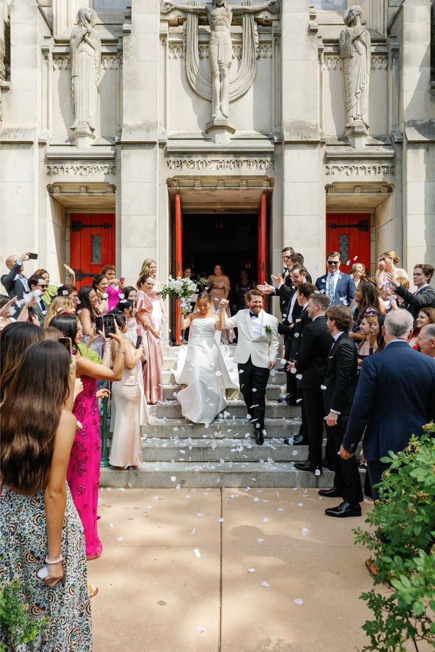 A celebratory wedding exit on church steps with guests showering the couple in confetti while three red doors stand behind.