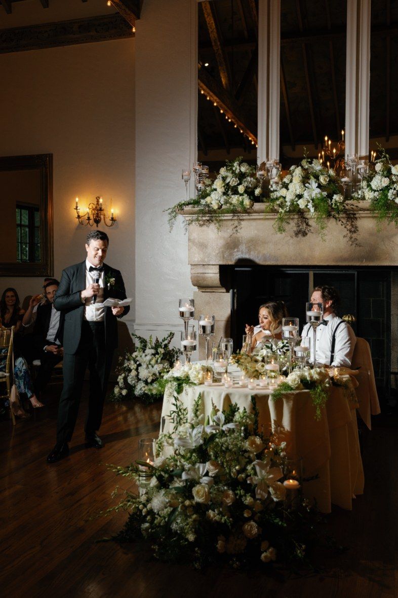 An elegant wedding reception with white floral arrangements and candlelight decor in a rustic venue.