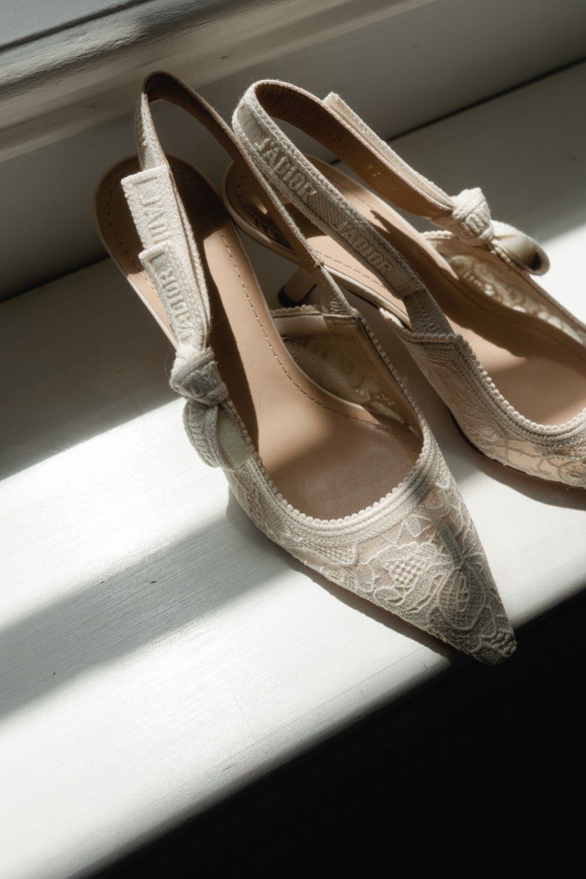 Delicate beige lace slingback shoes laying in dramatic window light and shadows.