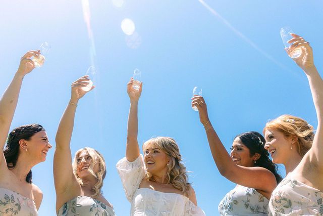 Group in formal attire raising champagne glasses against a bright blue sky.