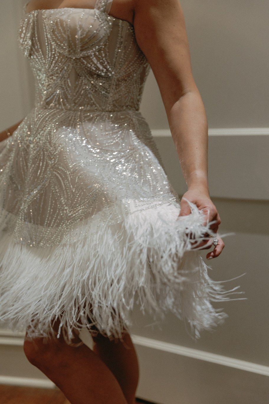 A white feathered mini dress with delicate details and wispy ostrich feather trim along the hemline sways elegantly.